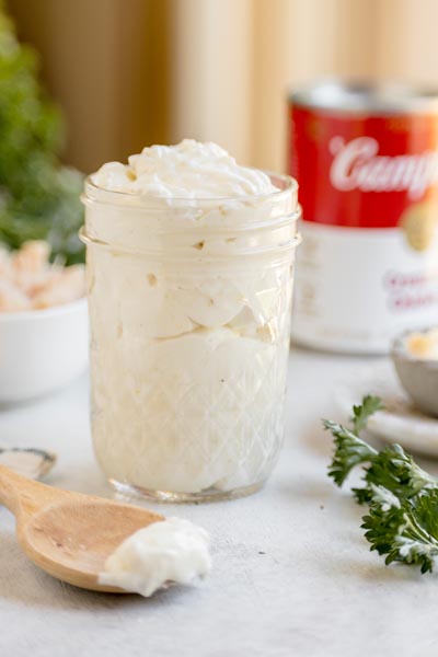 Keto condensed cream of chicken soup served in a glass jar with a wooden spoon and fresh herbs.