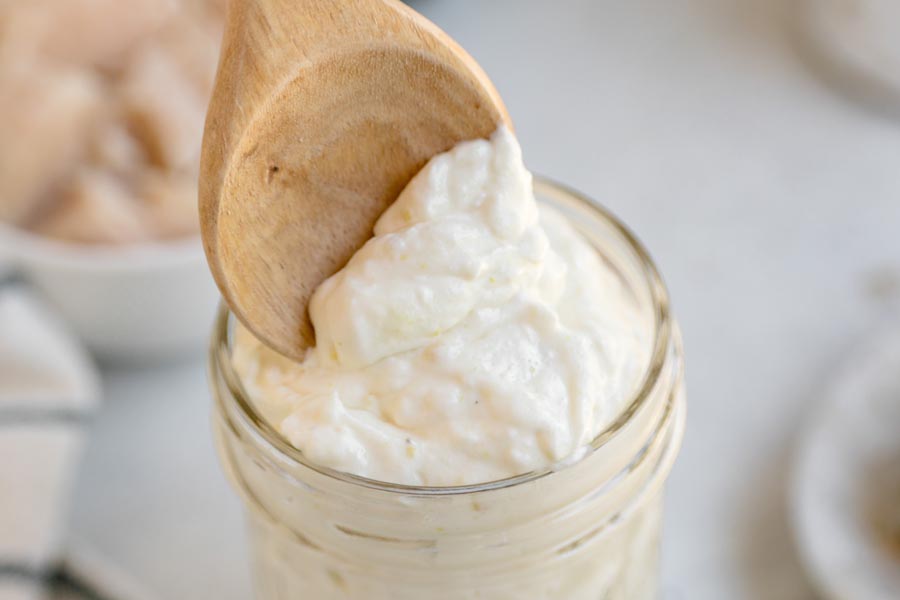 A wooden spoon scooping thick homemade keto cream of chicken soup from a glass jar.
