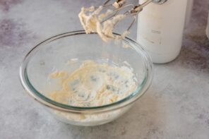 Softened cream cheese being whipped with a hand mixer until smooth for homemade cream of chicken soup.