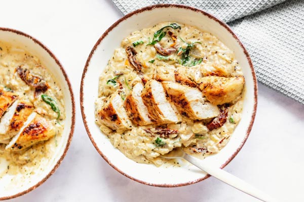 creamy italian chicken dish over caulilfower rice on two plates