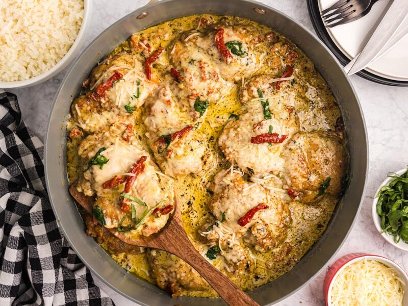 A skillet of creamy and cheesy topped pesto chicken with sun dried tomato on top.