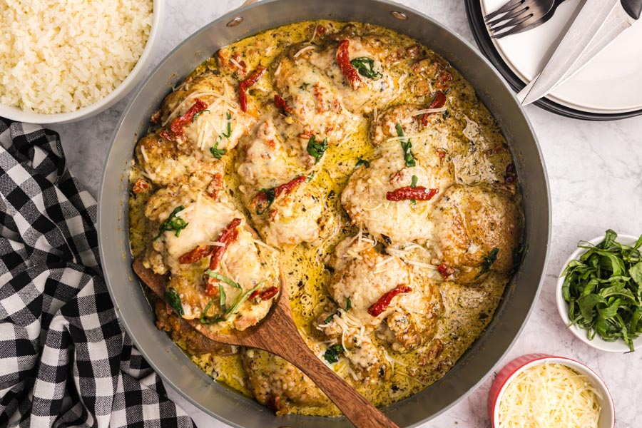 A skillet of creamy and cheesy topped pesto chicken with sun dried tomato on top.