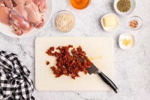 Chopped sun-dried tomatoes on a cutting board with a knife.