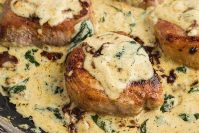 A pan seared pork chop topped with a creamy sauce with wilted spinach and crumbled bacon.