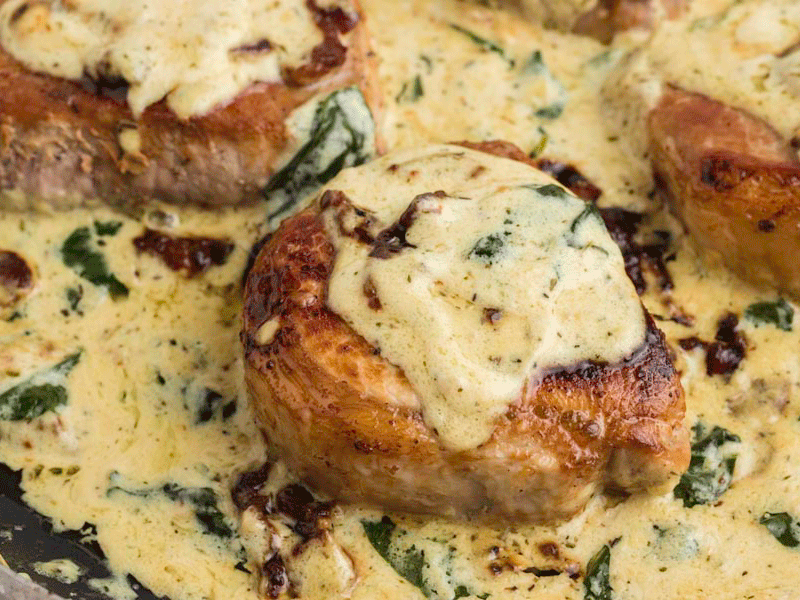 A pan seared pork chop topped with a creamy sauce with wilted spinach and crumbled bacon.