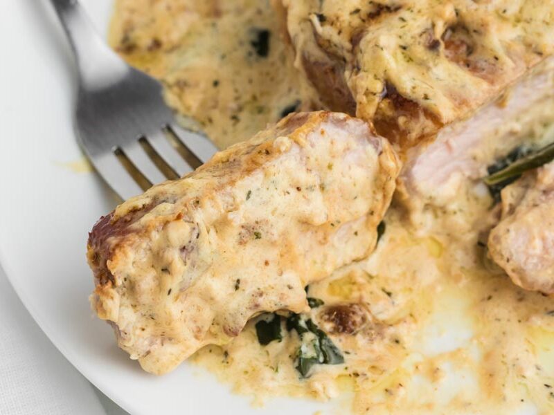 A slice of gravy coated pork chop on a plate with a fork through it.