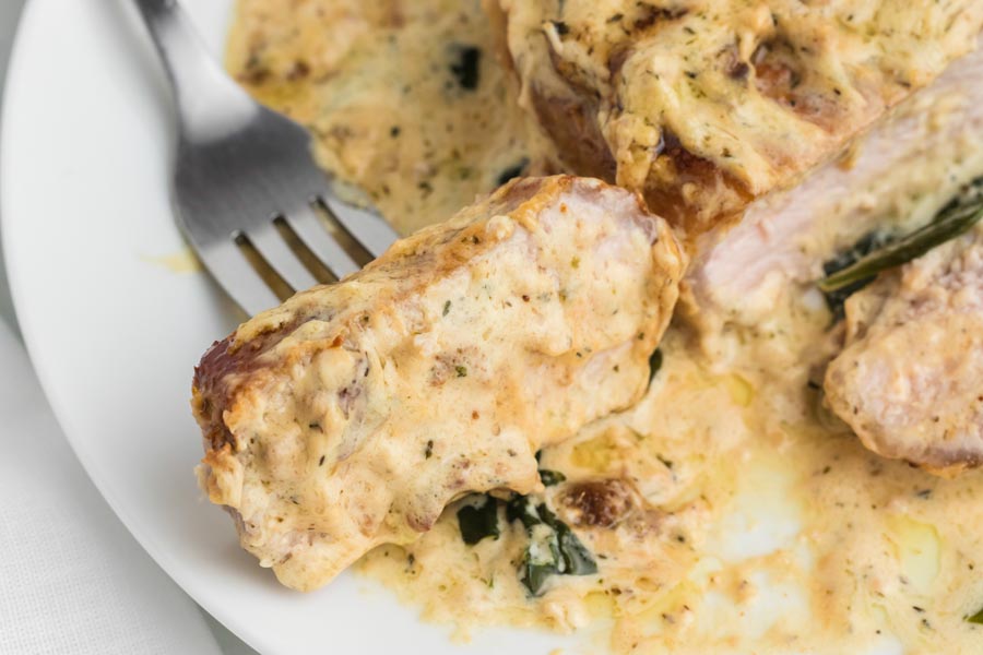 A slice of gravy coated pork chop on a plate with a fork through it.