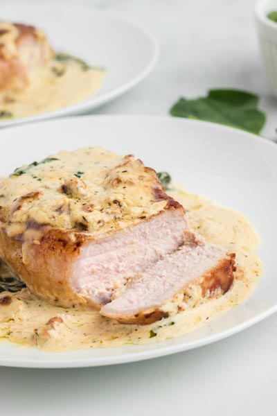 A plate with a slice off a pork chop showing the juicy interior sits on a pool of creamy sauce.