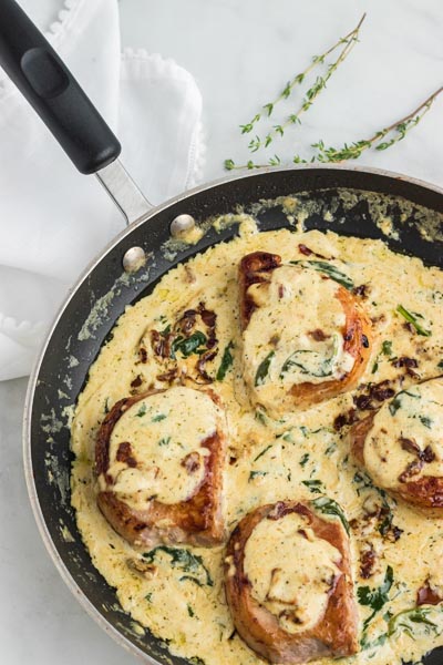 A skillet with creamy pork chops mixed with spinach, thyme and bacon.