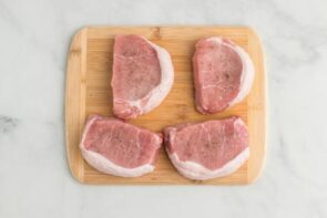 Four thick cut boneless pork chops on a wooden cutting board.