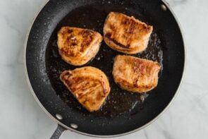 A skillet with golden, pan-seared pork chops inside.