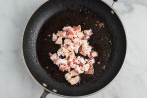 Chopped bacon cooking in a black skillet.