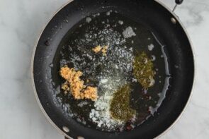 A black skillet with melted butter and chopped garlic cooking.