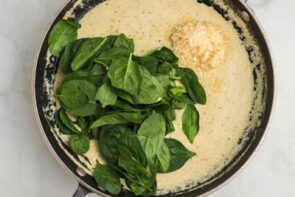 Fresh baby spinach leaves and parmesan cheese on top of a cream sauce in a skillet.