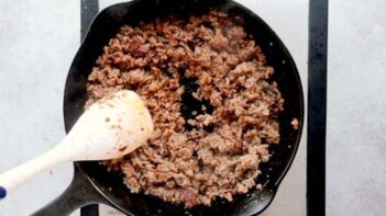 stirring cooked sausage with a white spatula