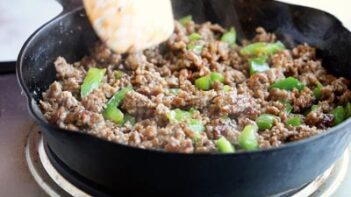 green bell pepper cooked in with browned sausage in a skillet on a burner