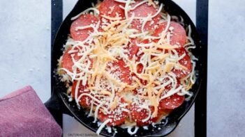 a cast iron skillet with uncooked pizza in it pepperoni topped with shredded cheese