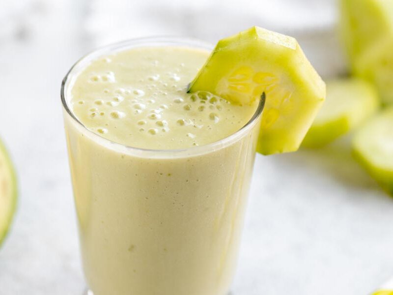 close up of a creamy green smoothie with a slice of cucumber on the rim of the glass