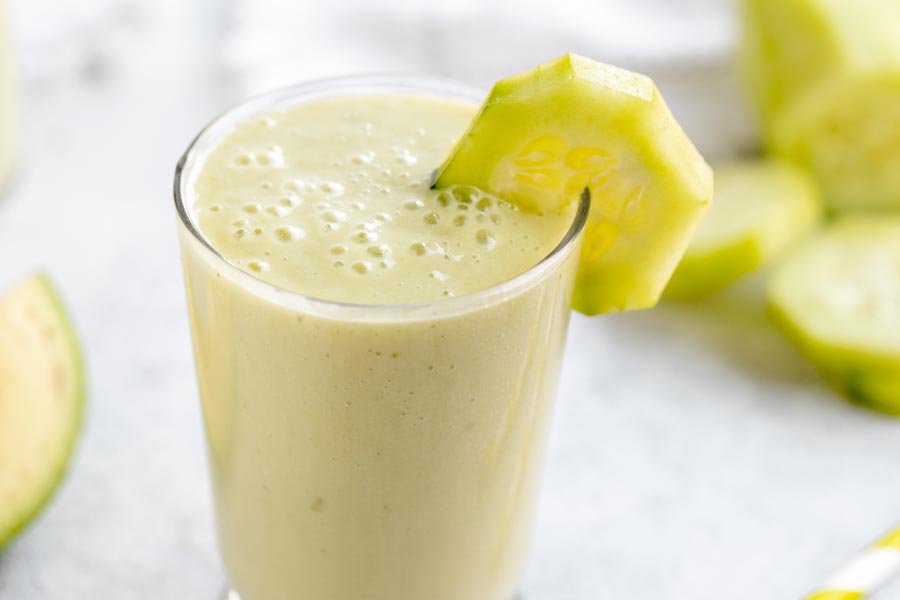 close up of a creamy green smoothie with a slice of cucumber on the rim of the glass