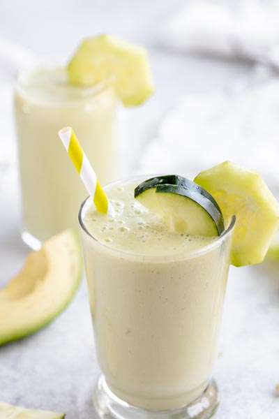 a glass filled with a cucumber smoothie with bubbles on top and slices of cucumber on the edge of the glass