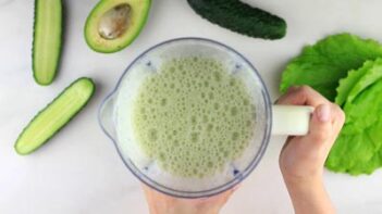 holding a blender filled with a green smoothie