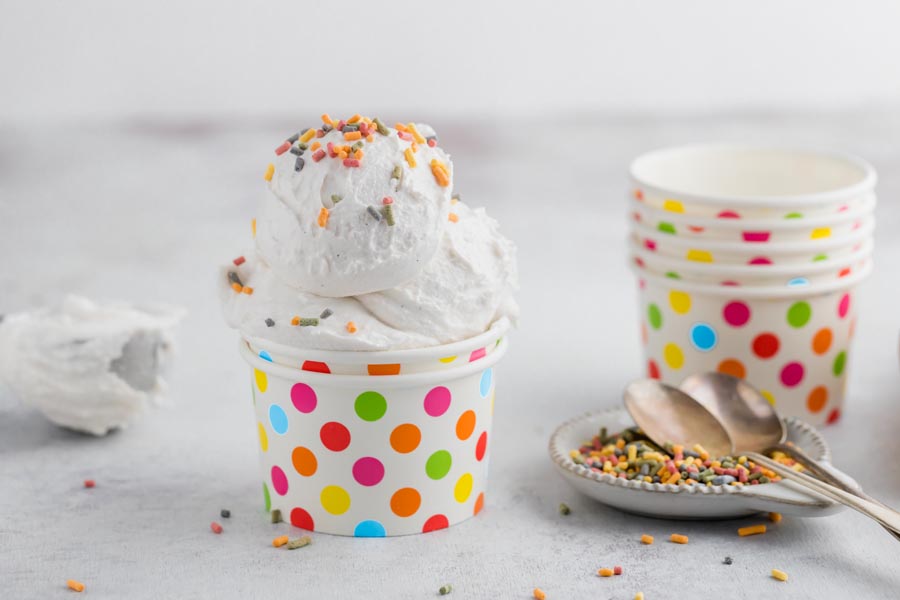 a multi-colored polka dotted cup with vanilla ice cream topped with colorful sprinkles