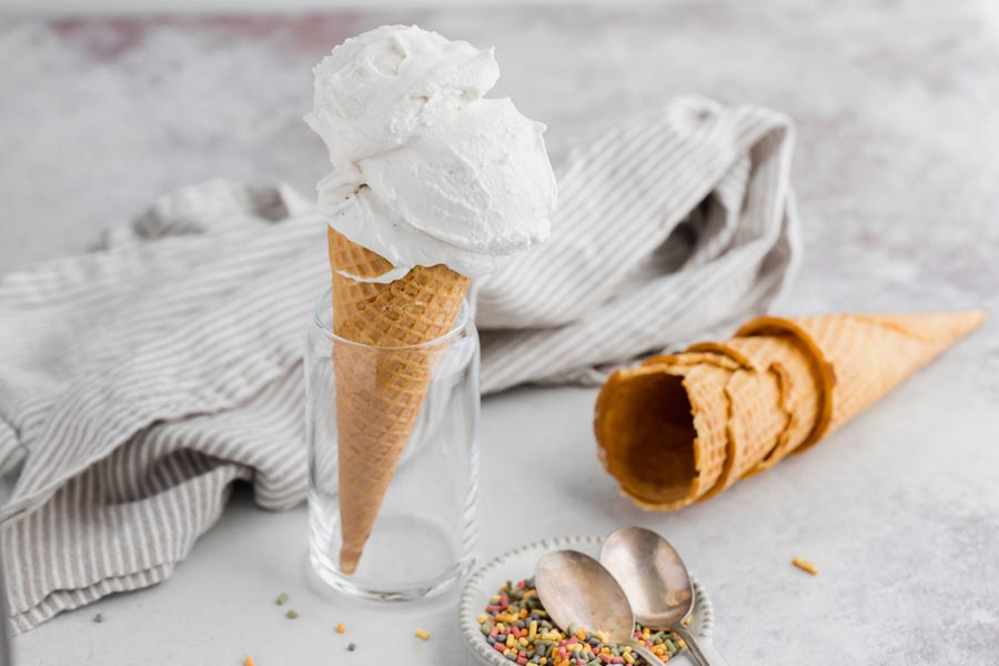 a vanilla cone next to more cones and a dish with spoons and sprinkles