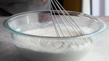 whisking coconut milk in a bowl with a wire whisk