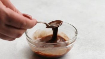 melted chocolate in a small glass dish dripping from a spoon
