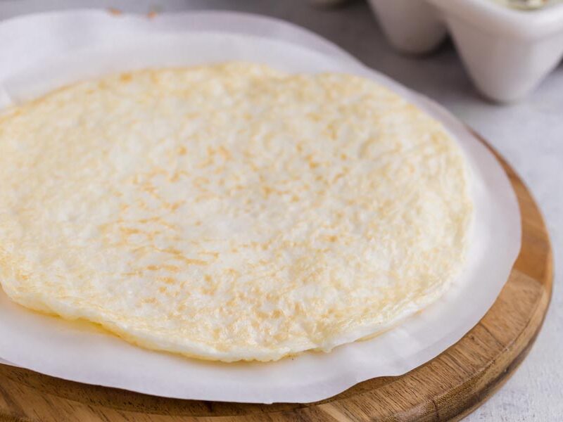 An egg white wrap on a circle of parchment paper and on top of a cutting board.