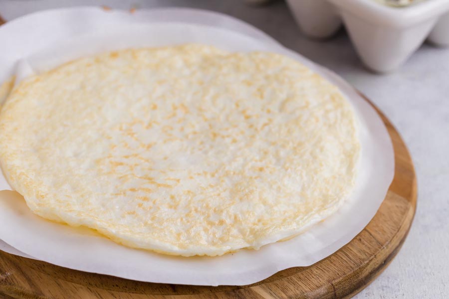 An egg white wrap on a circle of parchment paper and on top of a cutting board.