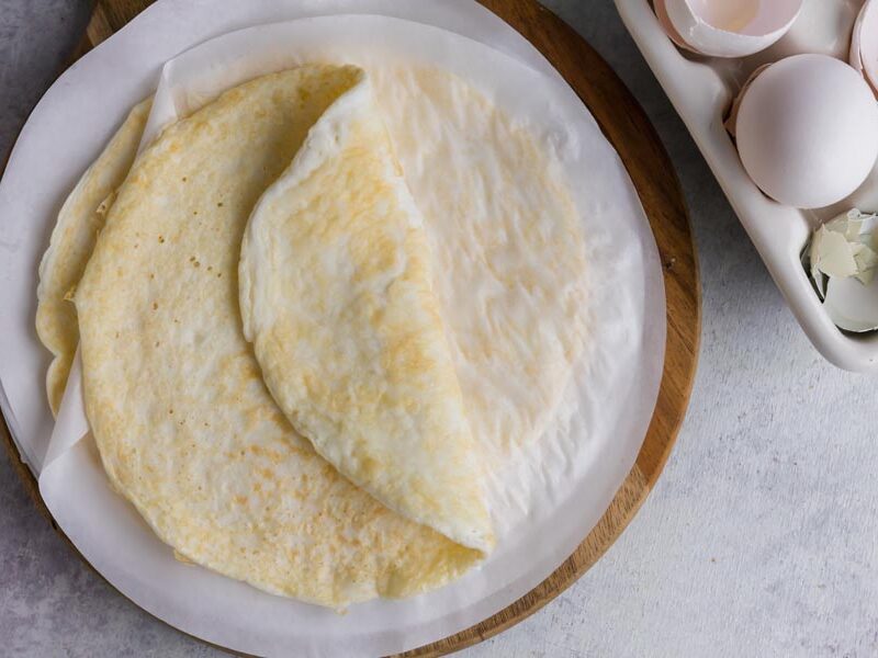 A wrap made of egg folded on itself on parchment paper next to cracked egg shells.