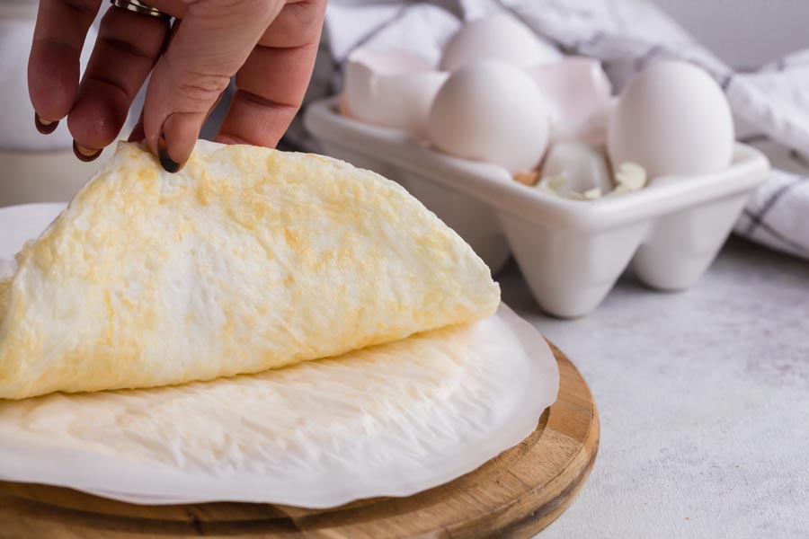 A hand peeling off an egg wrap from a piece of parchment paper.