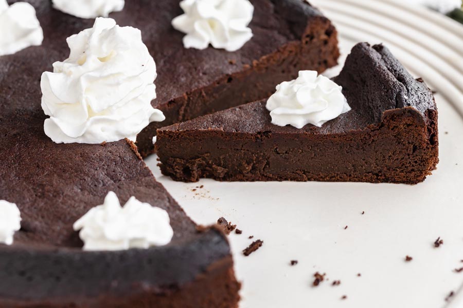 a thin slice of dense chocolate cake part of the whole cake and topped with whipped cream