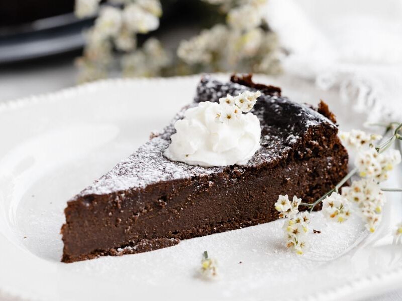 a slice of chocolate cake on a plate dusted with powdered sugar and topped with whipped cream baby's breath flowers lie beside