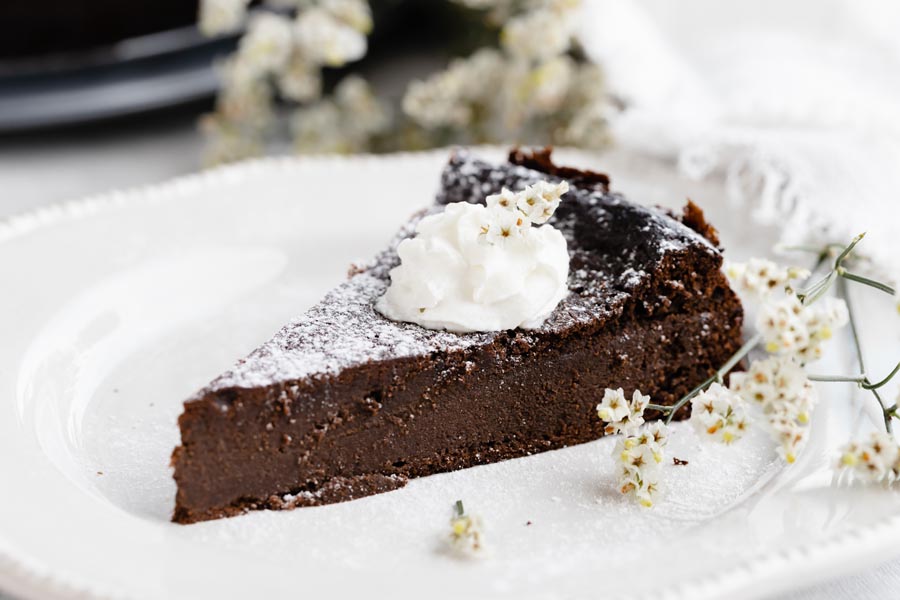 a slice of chocolate cake on a plate dusted with powdered sugar and topped with whipped cream baby's breath flowers lie beside