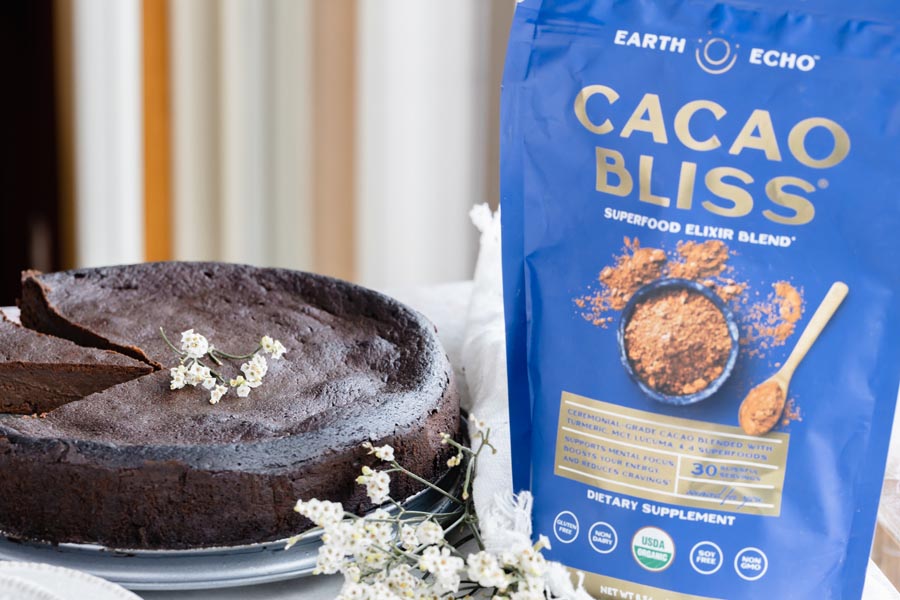 a blue bag of cacao bliss sits next to a whole chocolate cake topped with white flowers