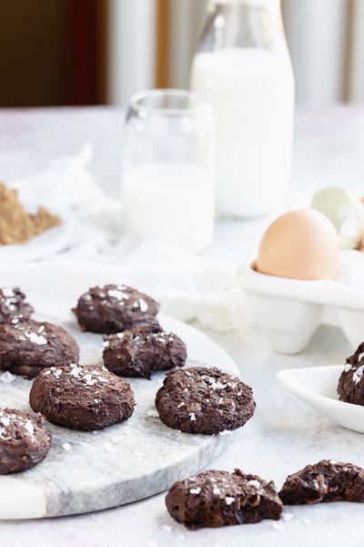 a bunch of chocolate cookies sitting on a marble block with eggs and milk in the background