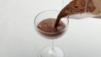 pouring a frozen chocolate drink into a stemmed glass