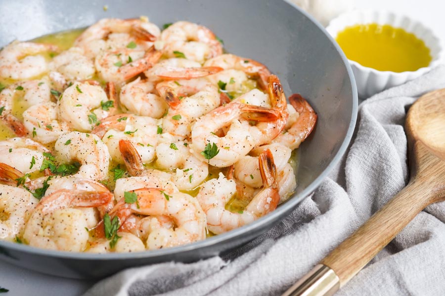 cooked shrimp in a pan topped with parsley and next to a spoon