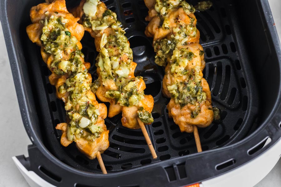 Three chicken skewers in an air fryer topped with a garlic sauce.