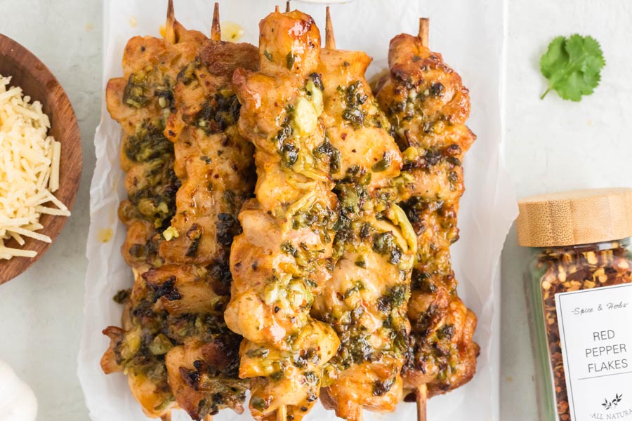 A plate of chicken skewers stacked on each other and coated with a cheesy garlic sauce.