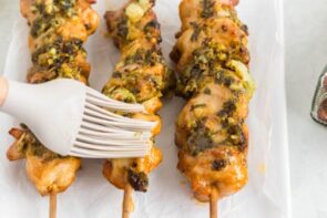 A silicone brush brushing garlic parmesan sauce on top of chicken skewers.