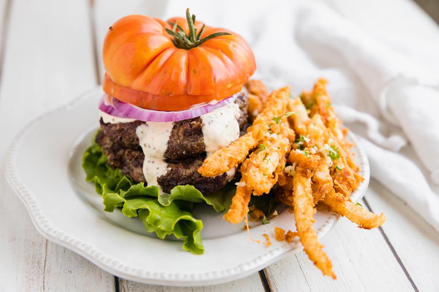 keto jicama fries on a plate next to a bunless burger with sauce dripping and a tomato on top