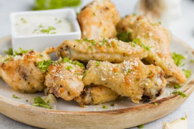 A pile of crispy wings coated with parmesan and parsley on a plate.