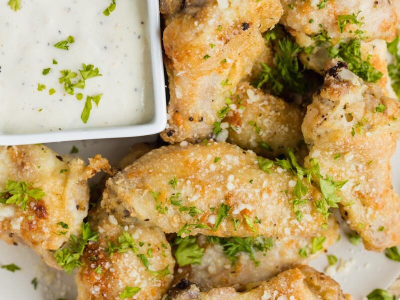 Garlic parmesan wings with grated parmesan and parsley beside a bowl of ranch.