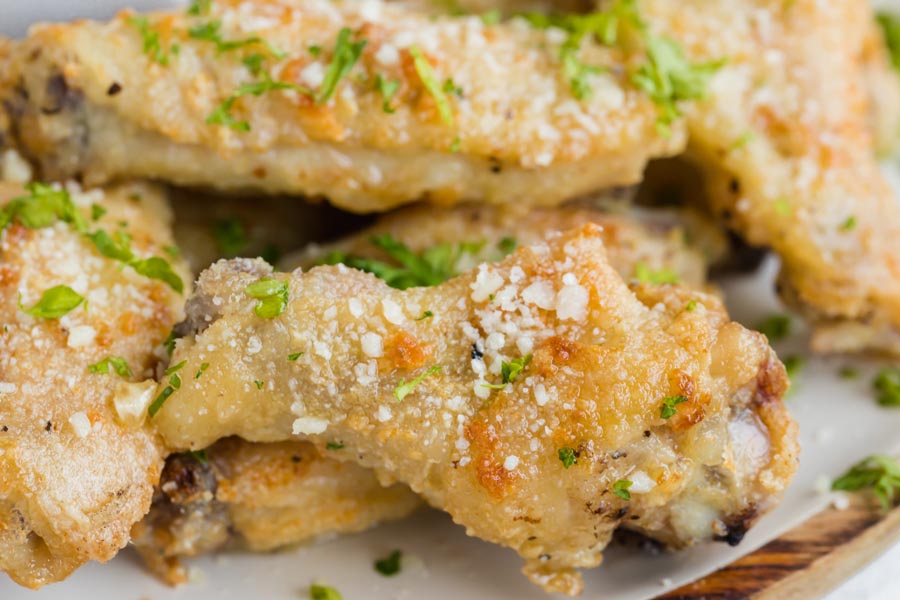 Close up of a crispy drumette wing topped with freshly grated parmesan and parsley.