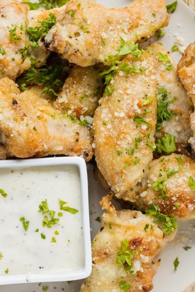 A pile of golden crispy wings on a plate next to ranch dressing and topped with parsley.