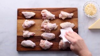 A hand patting wings with a folded paper towel.