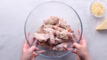 Hands tossing a bowl with wings.